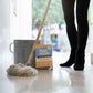 A person's legs next to a mop and bucket with Strip Wash floor cleaner packaging sitting next to it