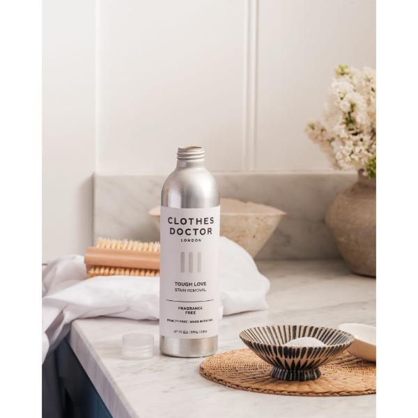 Clothes Doctor Tough Love stain removal in aluminium bottle on a marble countertop with brushes and soap alongside