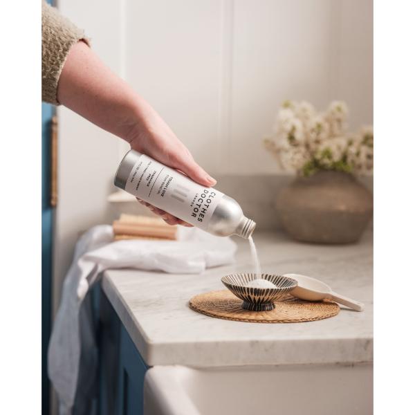 Person pouring Clothes Doctor Tough Love powder stain removal into bowl from aluminium bottle