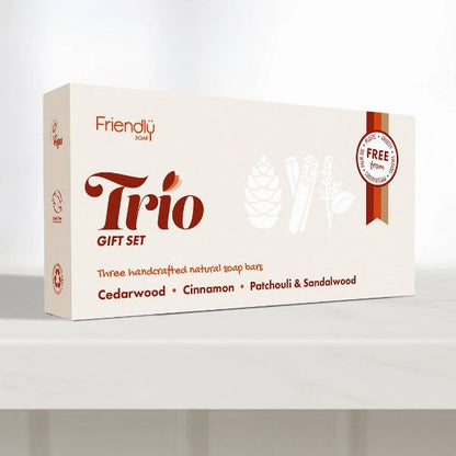 A boxed gift set labelled 'Friendly' Trio Gift Set, shown on a light grey surface against a pale grey background. The box is off-white with dark red and brown text and small white line drawings of natural ingredients.