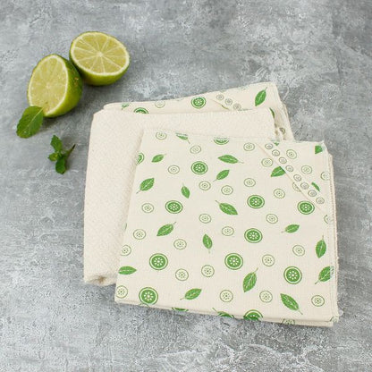 Set of organic cotton paper towels with green mint pattern on a marble background shown unwrapped next to sliced lime