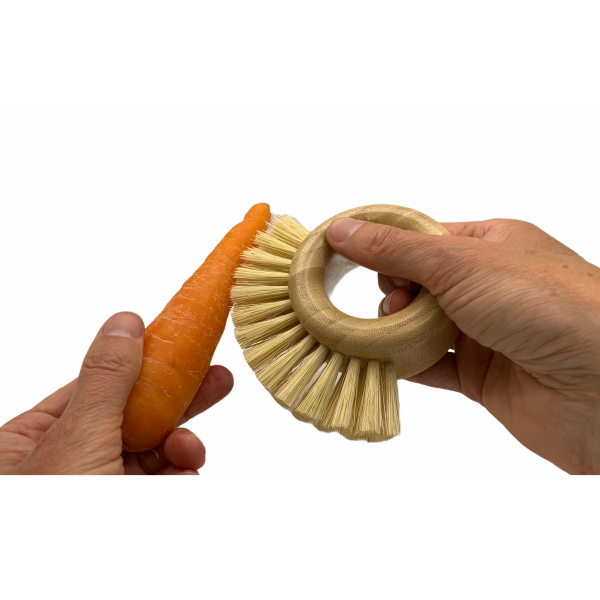 Bamboo vegetable brush in hand scrubbing a carrot