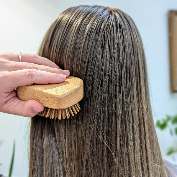 Person using wooden detangling hairbrush on their hair with a blurred background