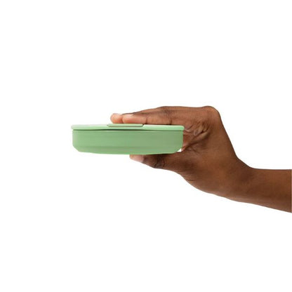 Collapsible cup shown collapsed in a hand in sage green