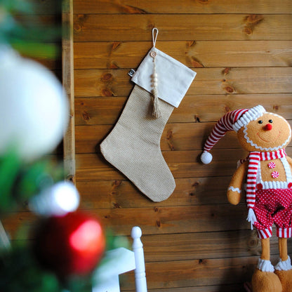 Natural jute eco-friendly Christmas stocking hanging on a wooden panel next to a Christmas tree and Christmas soft toy