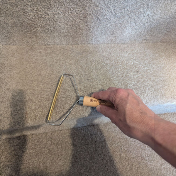 Wooden-handled metal tool lint and hair remover in use on a carpet