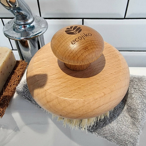 Wooden body brush with ecojiko logo on a bathroom counter next to soap