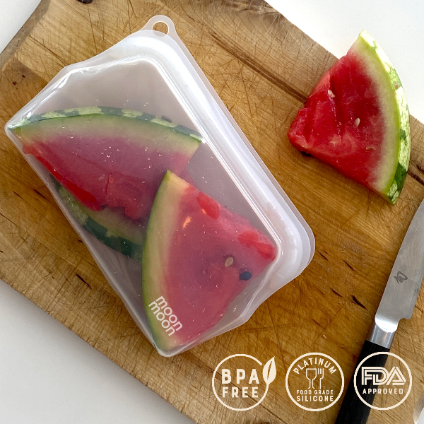 Watermelon slices in a silicone pouch on a wooden cutting board with 'Moon River' branding and certification logos.