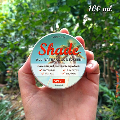 Hand holding a tin of Shade all-natural sunscreen with a green leafy background, with text reading "100ml"