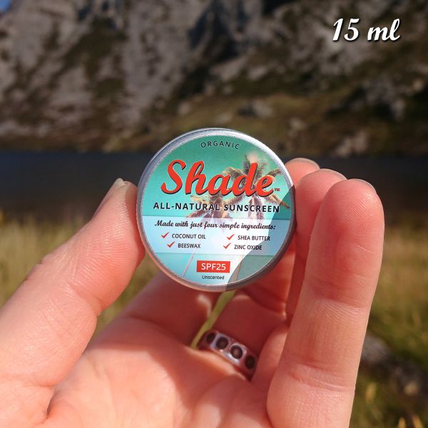 Hand holding a tin of Shade all-natural sunscreen with a green leafy background, with text reading "15ml"
