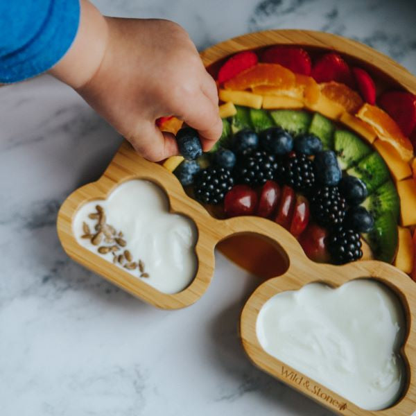 Eco-friendly baby bamboo plate with food and a child's hand picking a blueberry