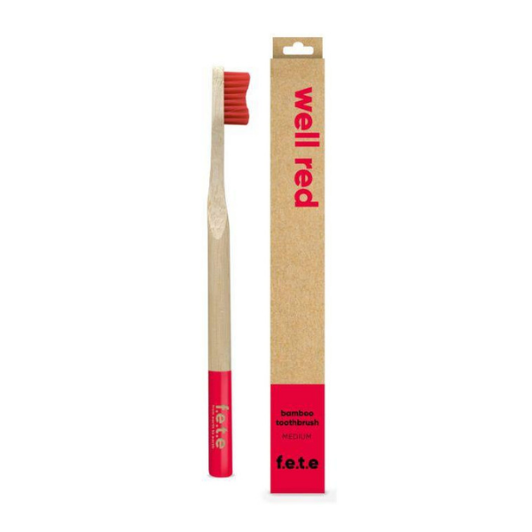 Bamboo toothbrush well red (red bristles and tip of brush) shown alongside cardboard box